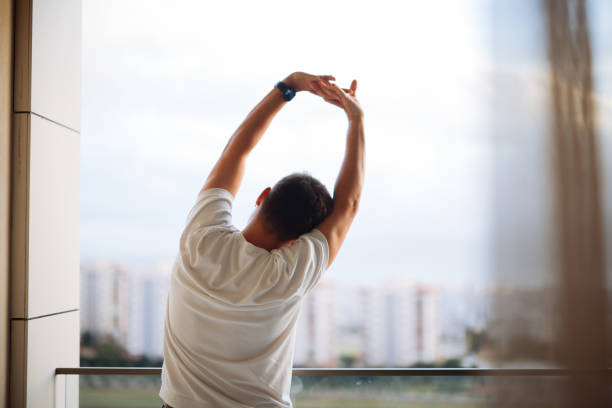 Someone standing near a window doing a gentle arm stretch during a quiet break